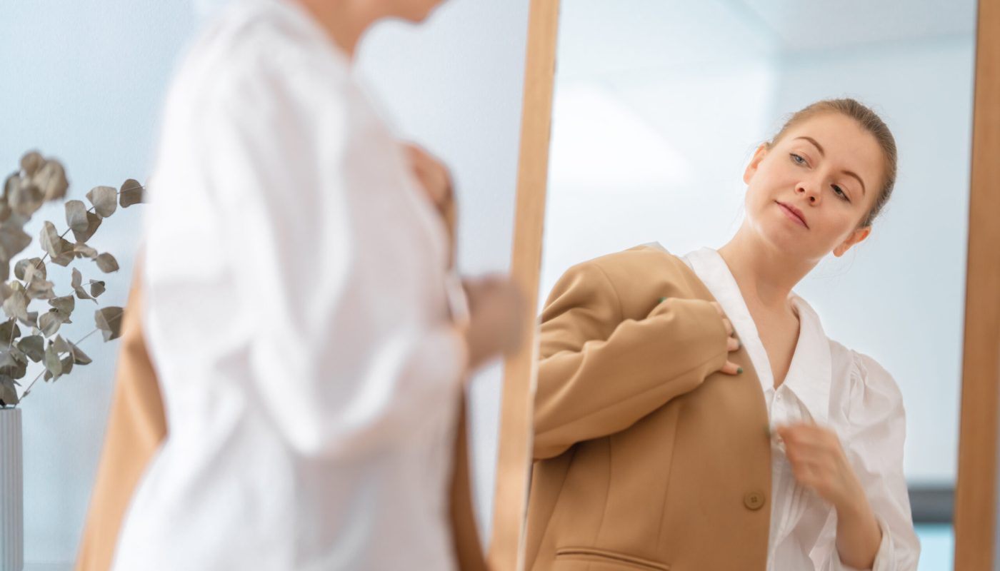 Self confident single woman looking at her reflection in mirror, putting on business clothes.